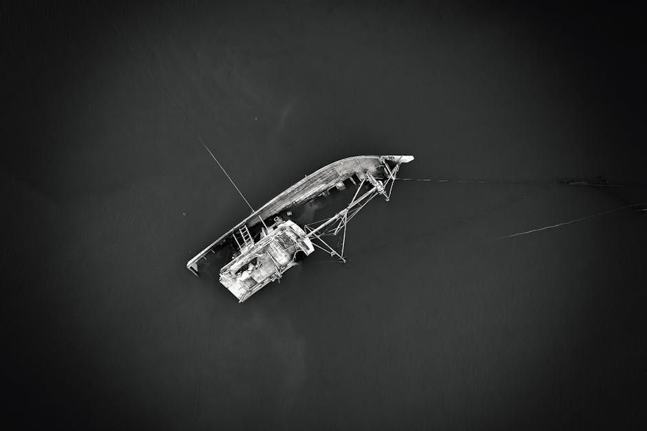 An aerial view of a weathered shipwreck partially submerged in dark waters, creating a dramatic scene.